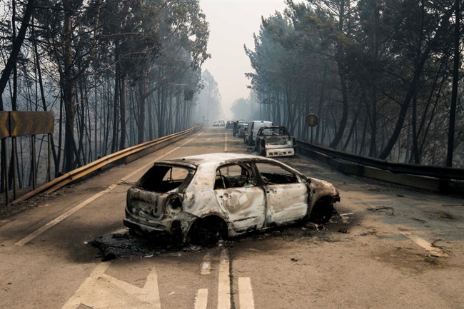 Rodovia com casco de um carro queimado, floresta e estrada também incendiadas