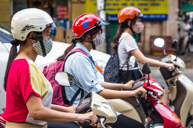 Mulheres no trânsito, guiando motos, com máscaras no nariz.
